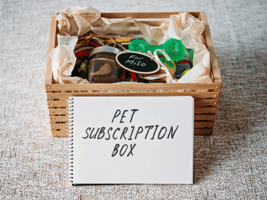 A wooden box containing pet toys and accessories labeled as "Pet Subscription Box."