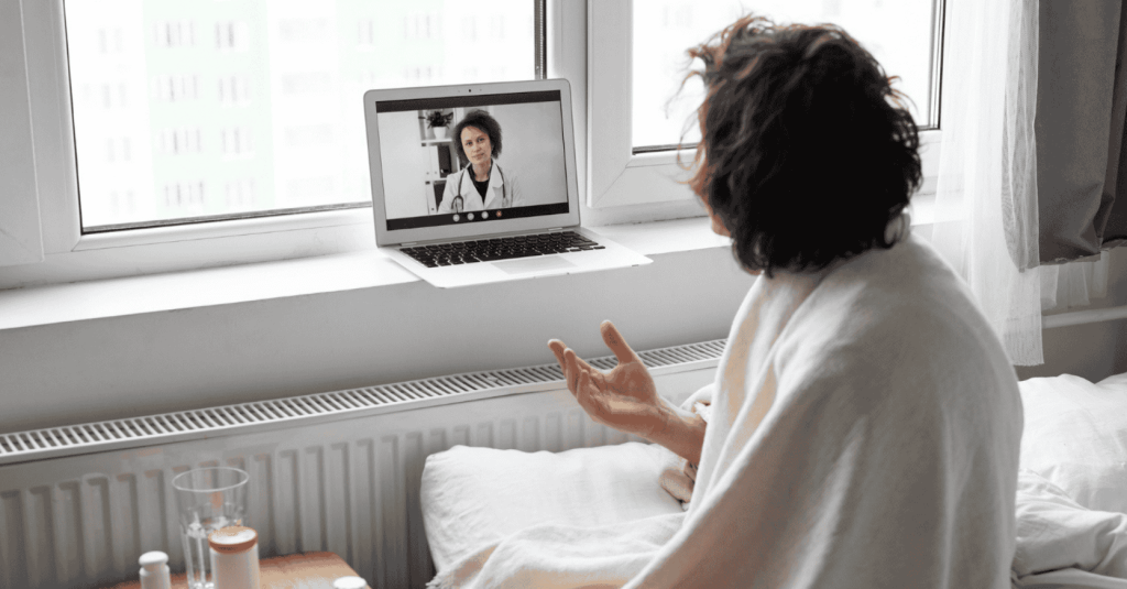 A person wrapped in a blanket speaks to a doctor during a virtual therapy session via a laptop screen.